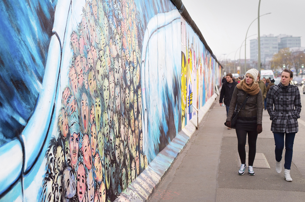 BERLIN, GERMANY - NOV 15, 2014: People walkingat Berlin Wall at East Side Gallery . It's a 1.3 km long part of original Wall which collapsed in 1989 and now is largest world graffiti gallery.